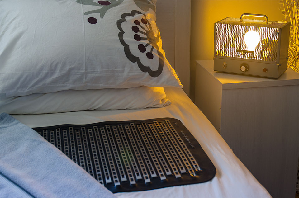 Tapis de détection d'urine installé dans un lit avec appareil avec alarme sonore et visuelle sur la table de chevets - Solution Pipi au lit de Méthode Urino-Arrêt